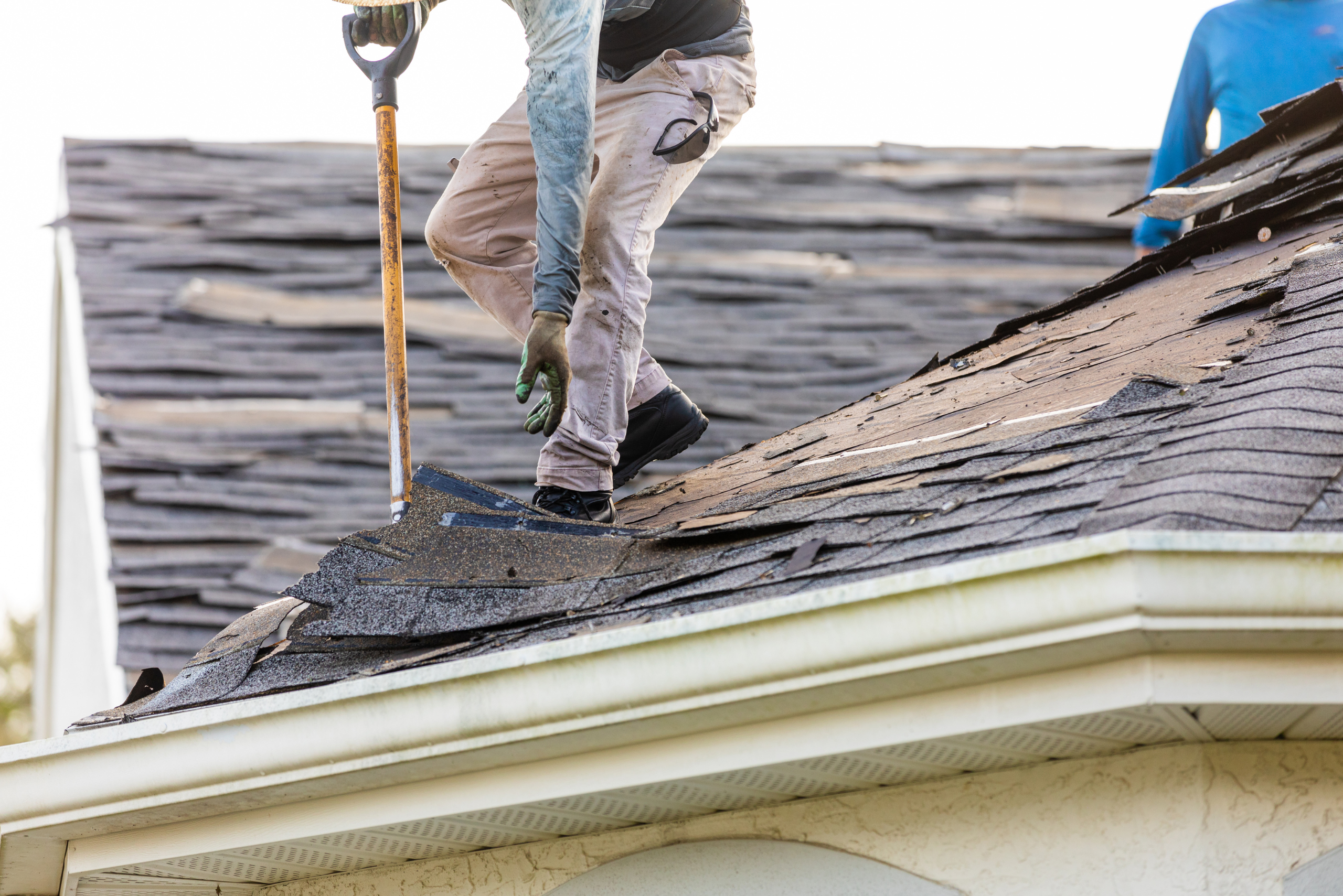 Roofer using a shovel to remove shingles.