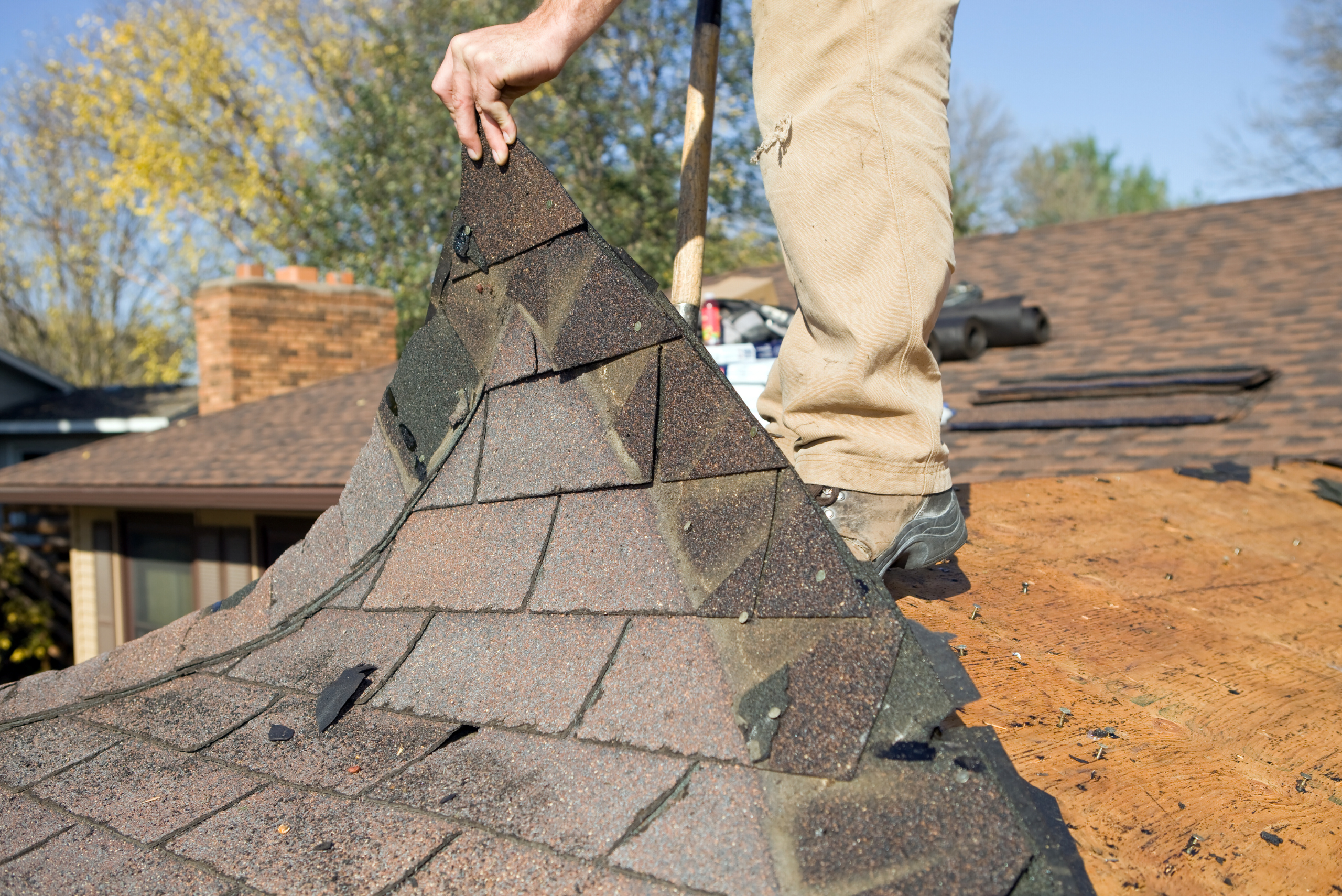 Roofer removing shingles from roof.