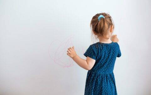 little girl drawing on wall with bright colored marker