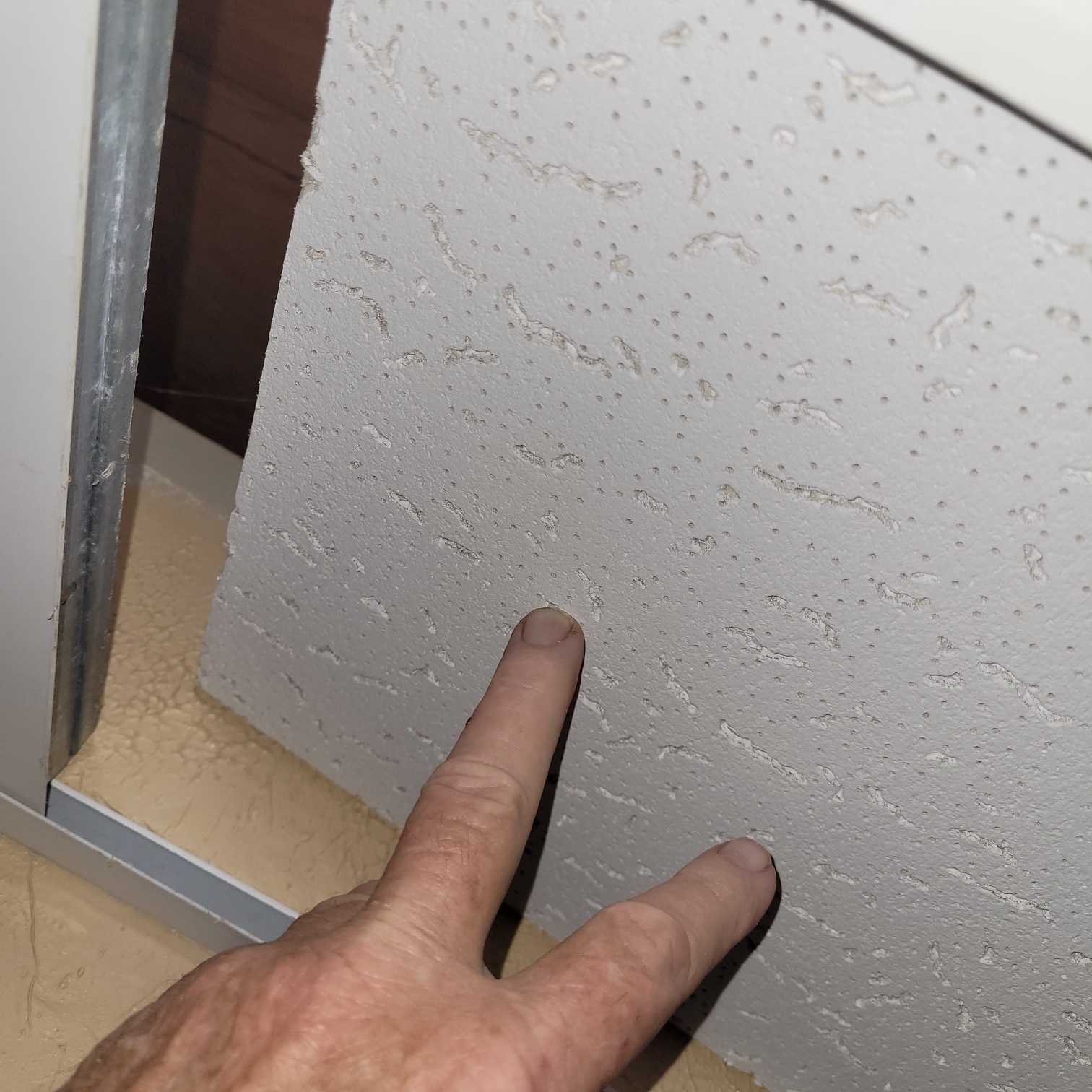 Closeup of hand lifting a drop ceiling tile.