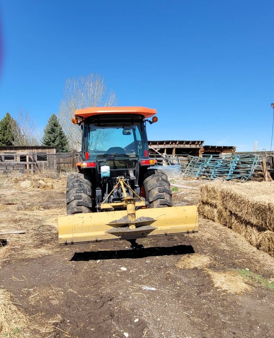 Tractor with a blade attachment on the rear near stacked hay bales.