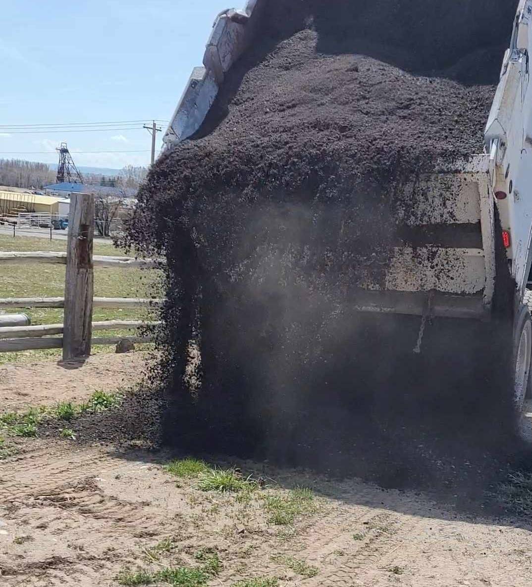 Dump truck unloaded crushed asphalt on a dirt lane.