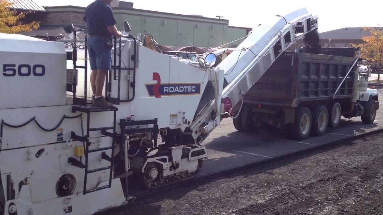 Heavy-duty machine removing asphalt, which is ramped into the bed of a dump truck.