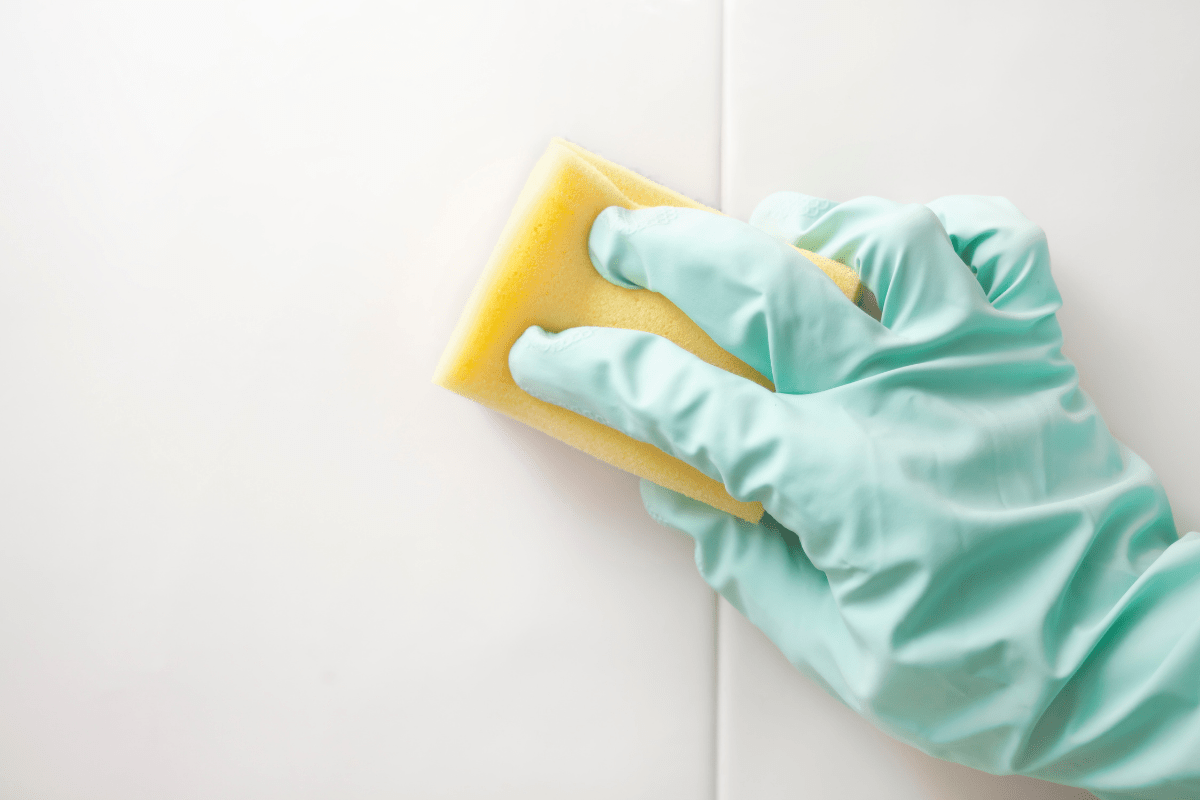 green glove hand cleaning white tile with yellow sponge