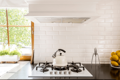 white subway tile backsplash in kitchen bright window in background oven range hood tea kettle