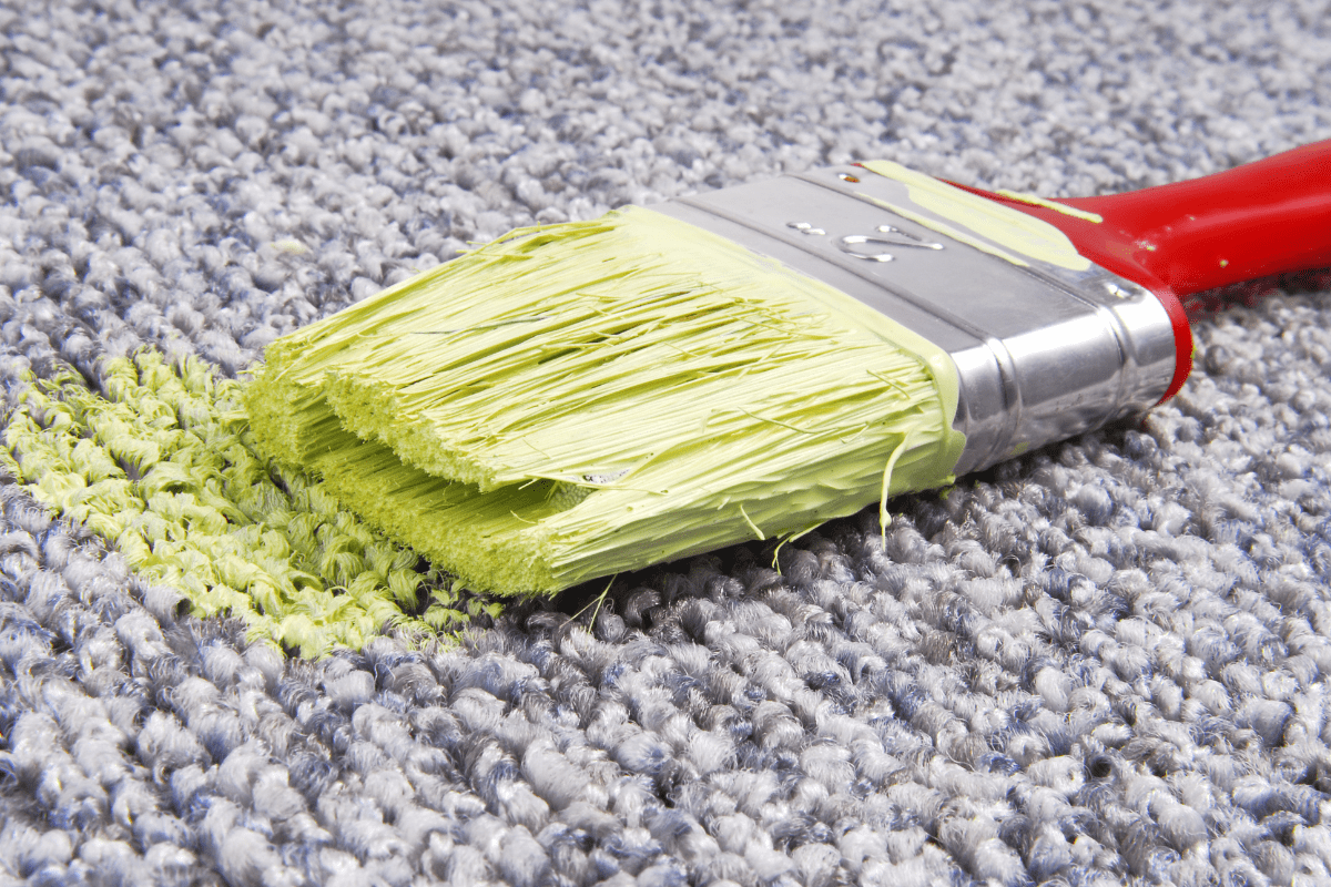lime green paint on red handled paint brush sitting on grey carpet
