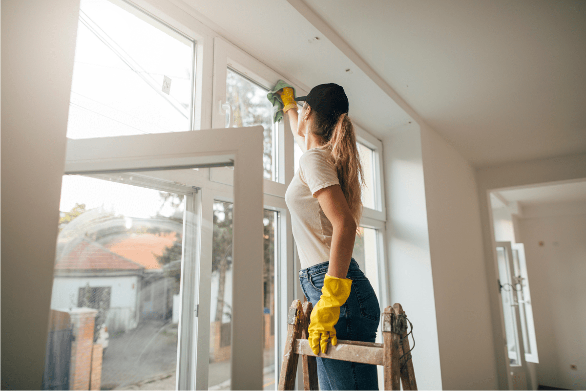 cleaning windows woman on ladder wearing hat and gloves