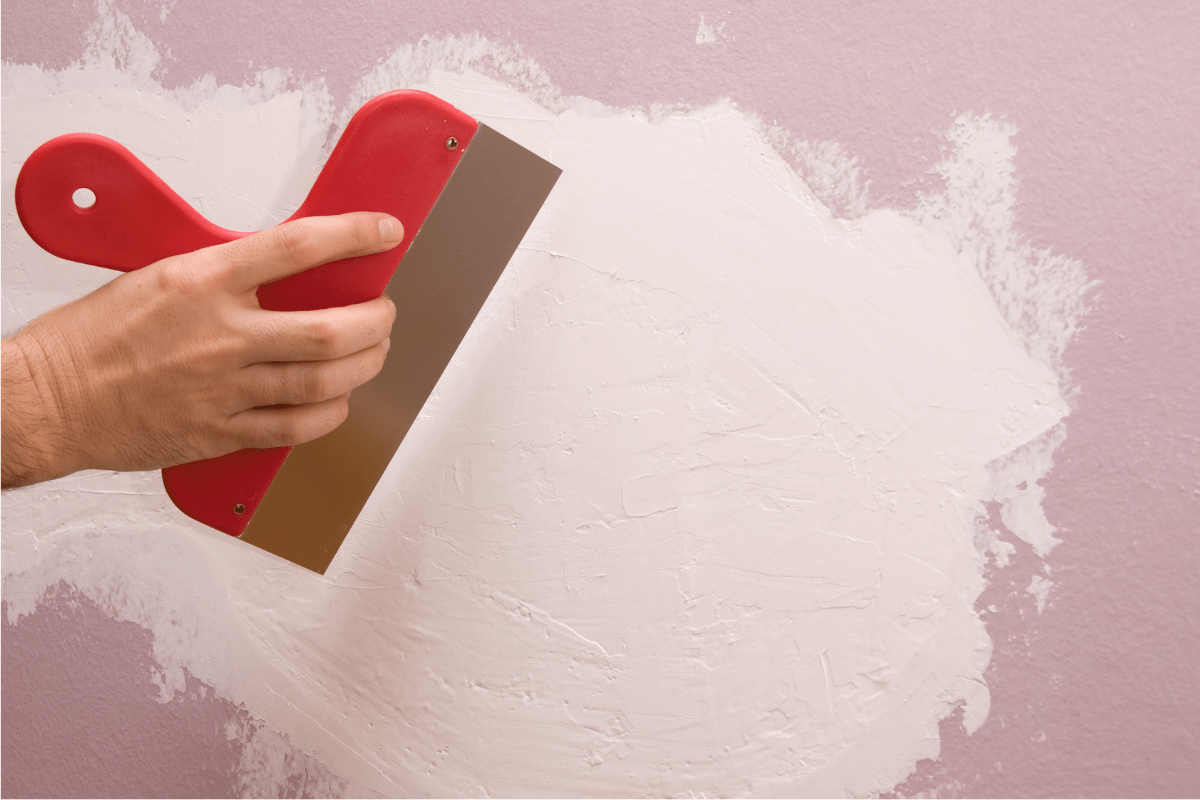 putty on pink wall red scraper hand