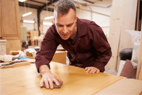 man in wood shop sanding piece of wood