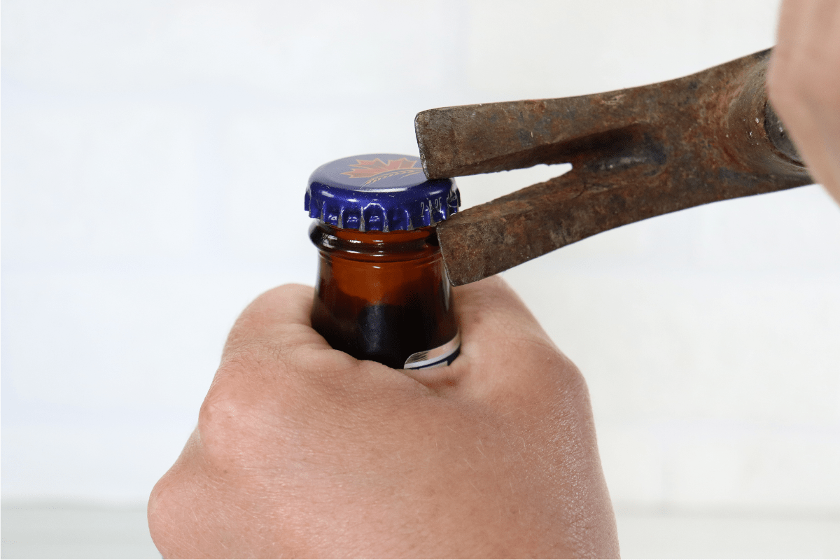 hand using rusty hammer to open beer bottle white background
