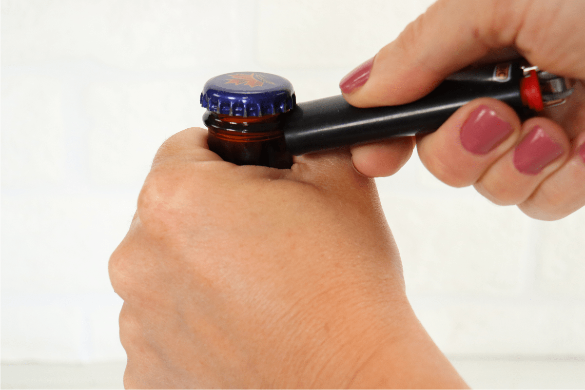 woman hand with pink nail polish using lighter to open beer bottle white background