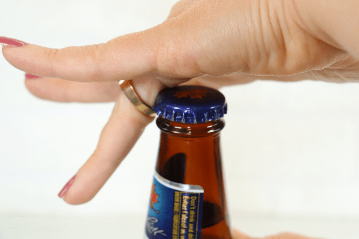 woman hand with pink nail polish using ring to open beer bottle white background
