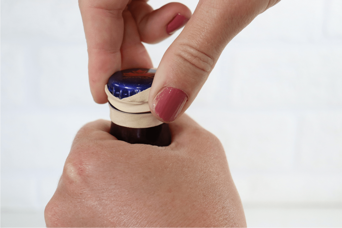 woman with pink nail polish using rubber band to open beer bottle white background