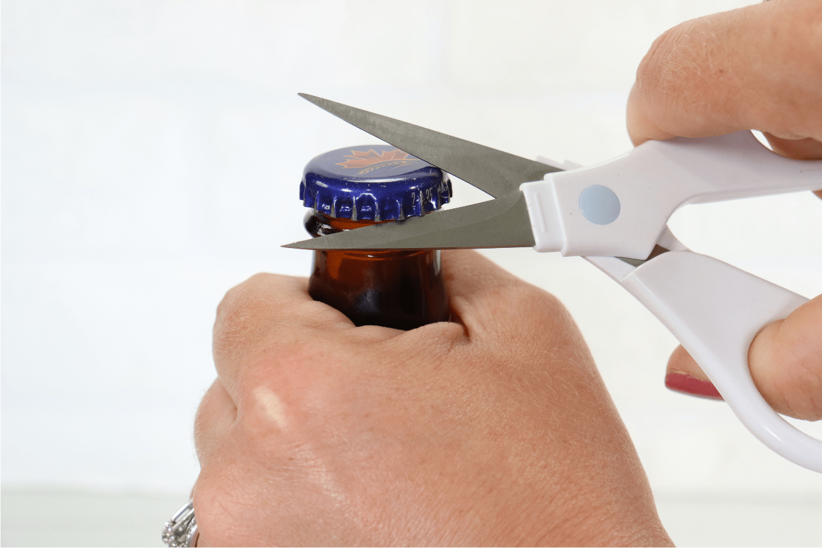 hand using scissors to open beer bottle white background