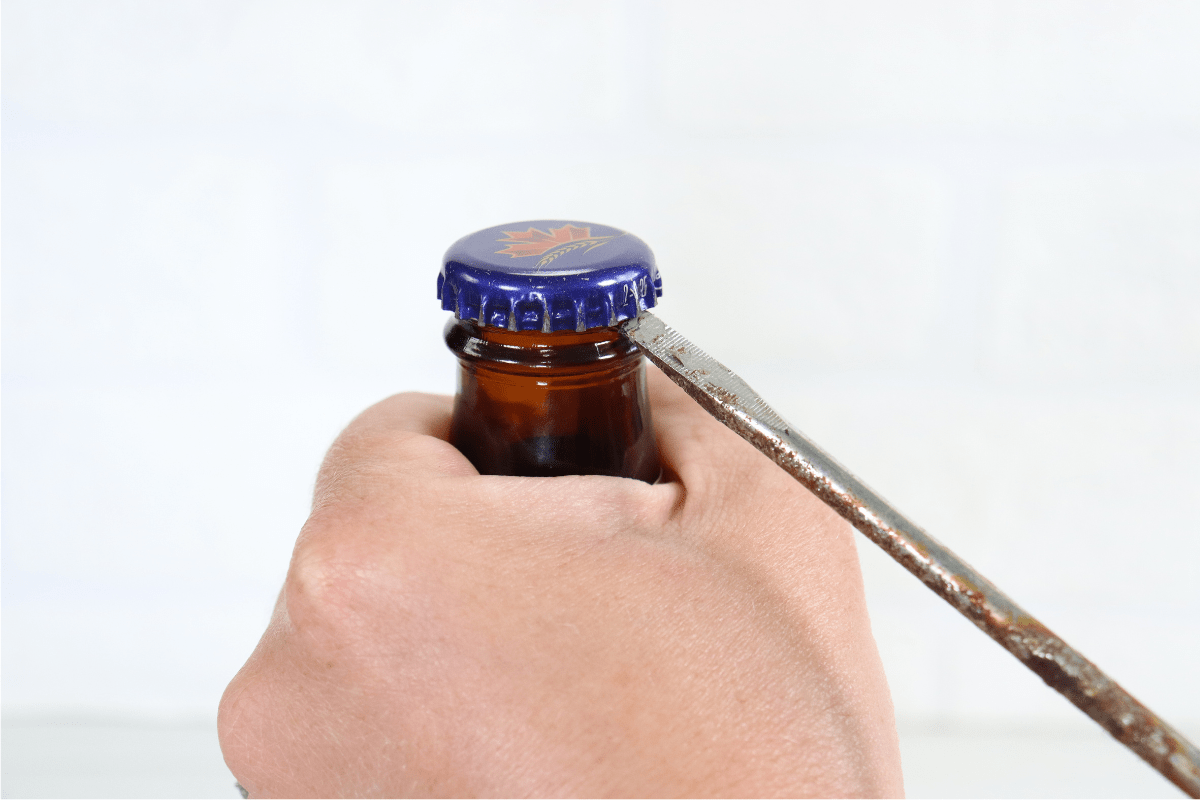 hand using flat head screwdriver to open beer bottle white background