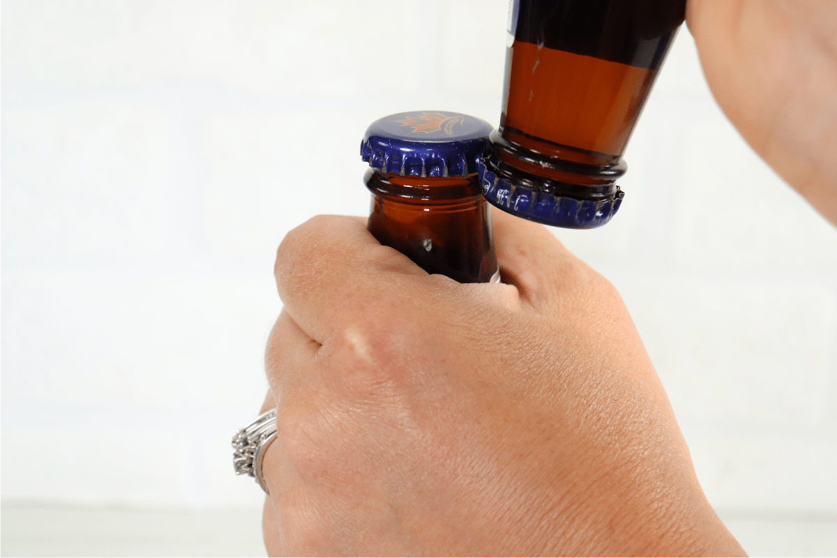 woman's hand using another beer bottle to open one beer white background