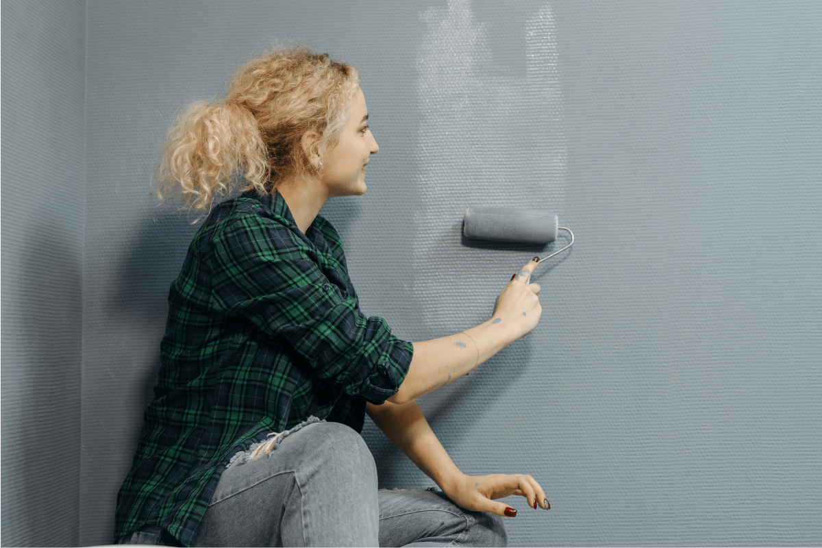 woman in plaid shirt painting wall grey roller