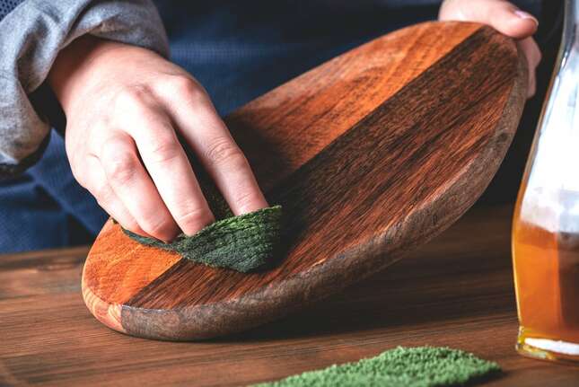 hardwood cutting board being wiped with green cloth close up