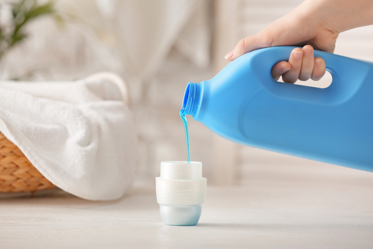 hand pouring out laundry detergent out of blue jug into small white cup