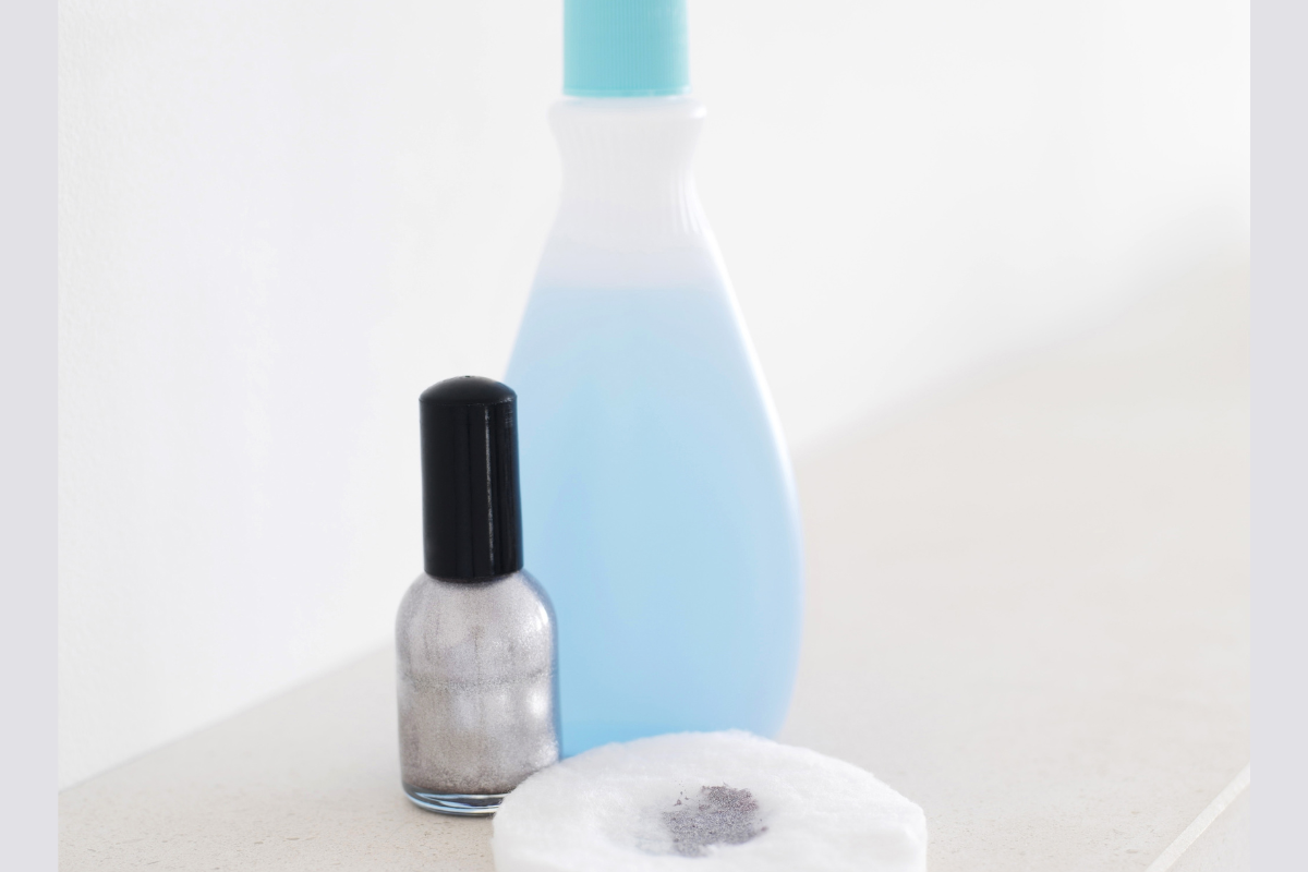 bottle of nail polish remover blue with grey sparkly nail polish and cotton pad
