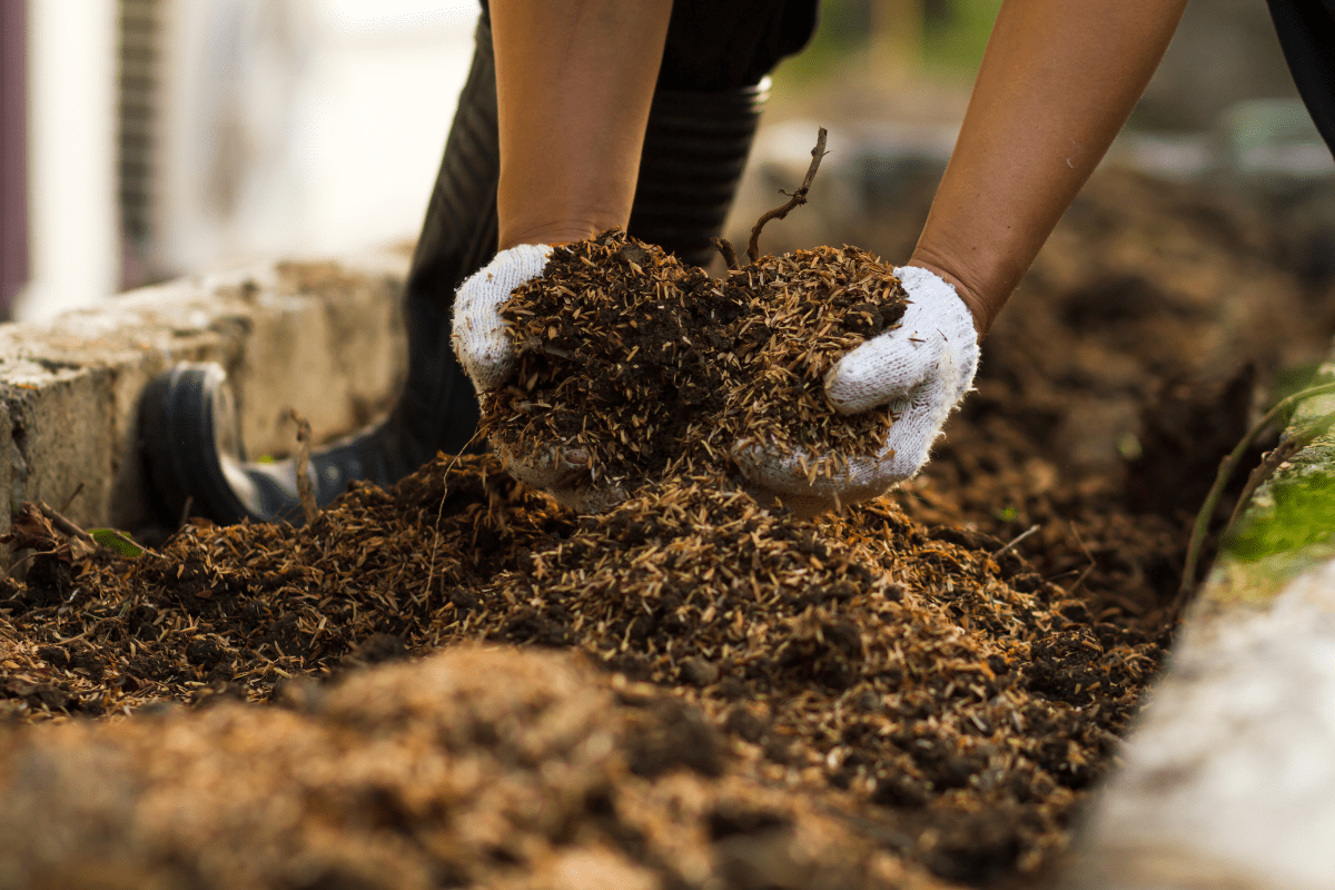 close up of hands grabbing a handful of soil mix wearing work gloves
