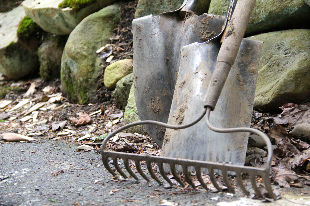 close up of dirty rake and shovels leaning on stones