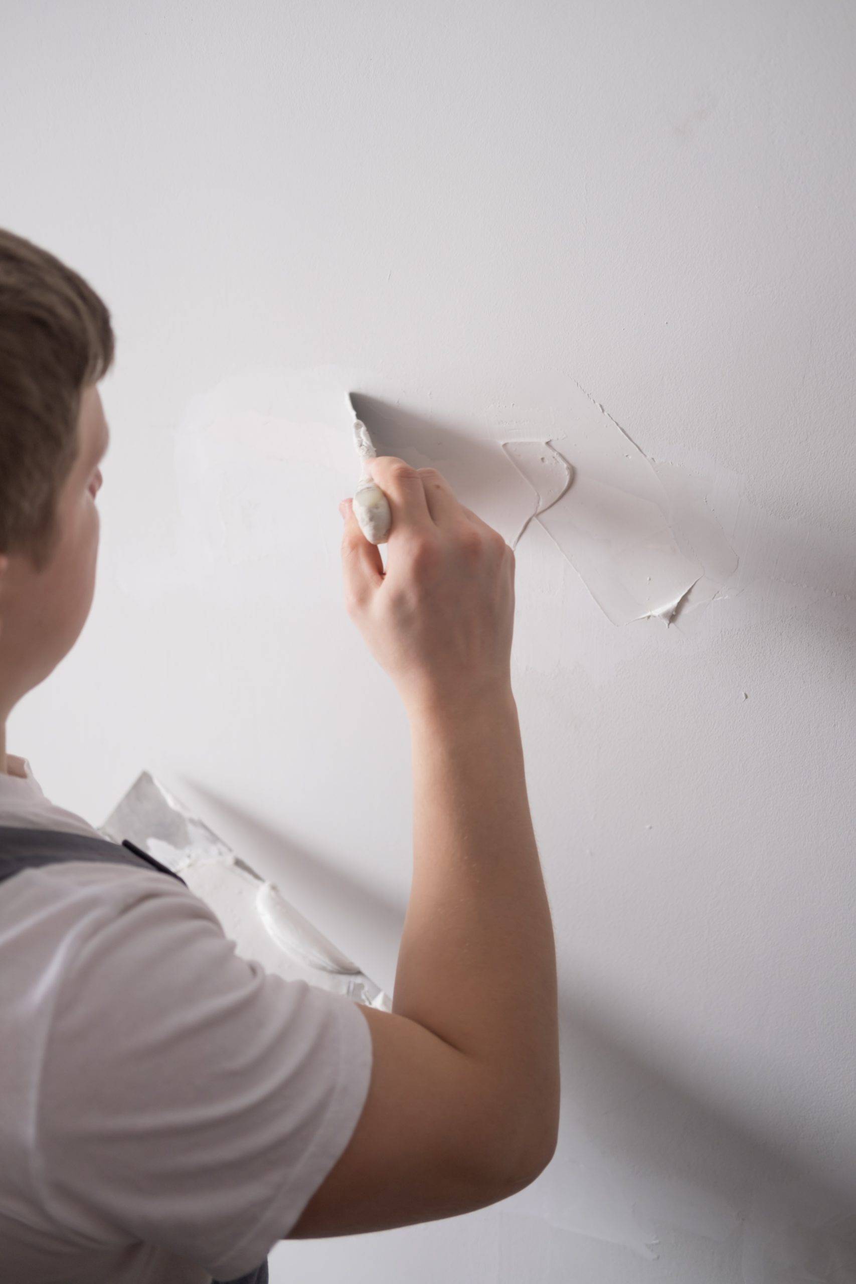 man patching hole in wall with putty and spackle