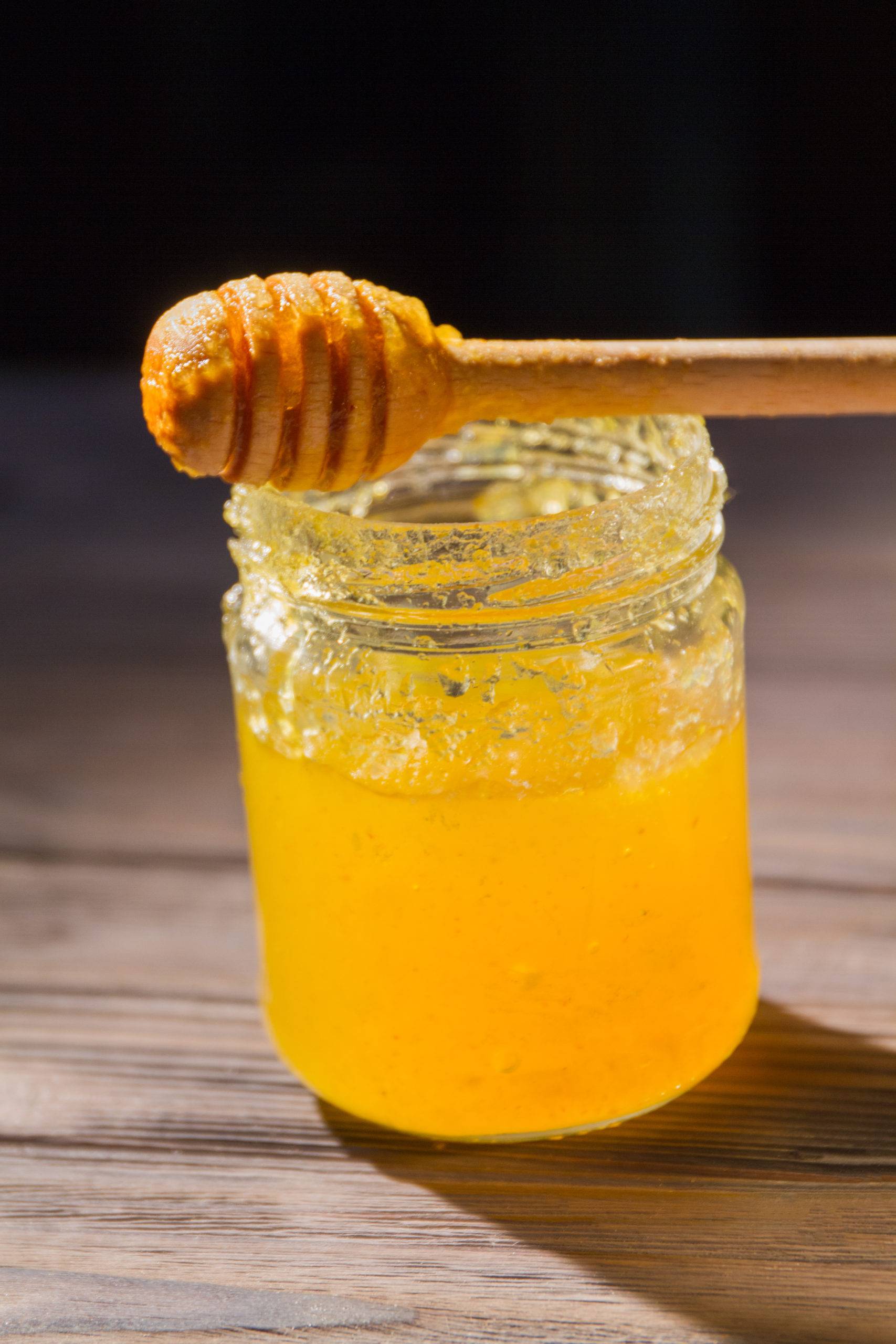 Vertical shot of glass jar of honey and wooden dipper. Honey composition close-up.