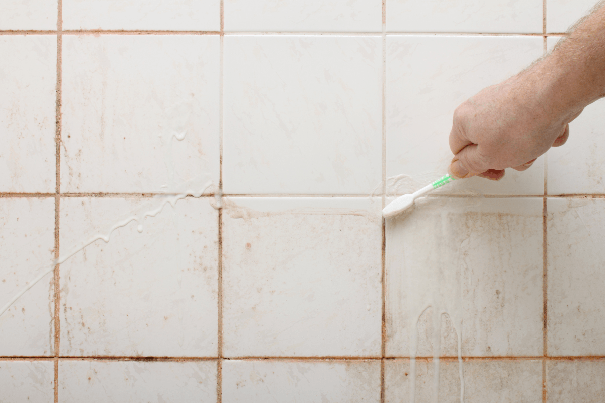 close up of hand scrubbing dirty tile shower wall with toothbrush