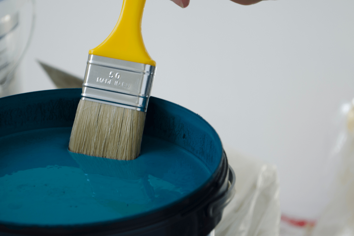close up of yellow handle paint brush in blue paint can