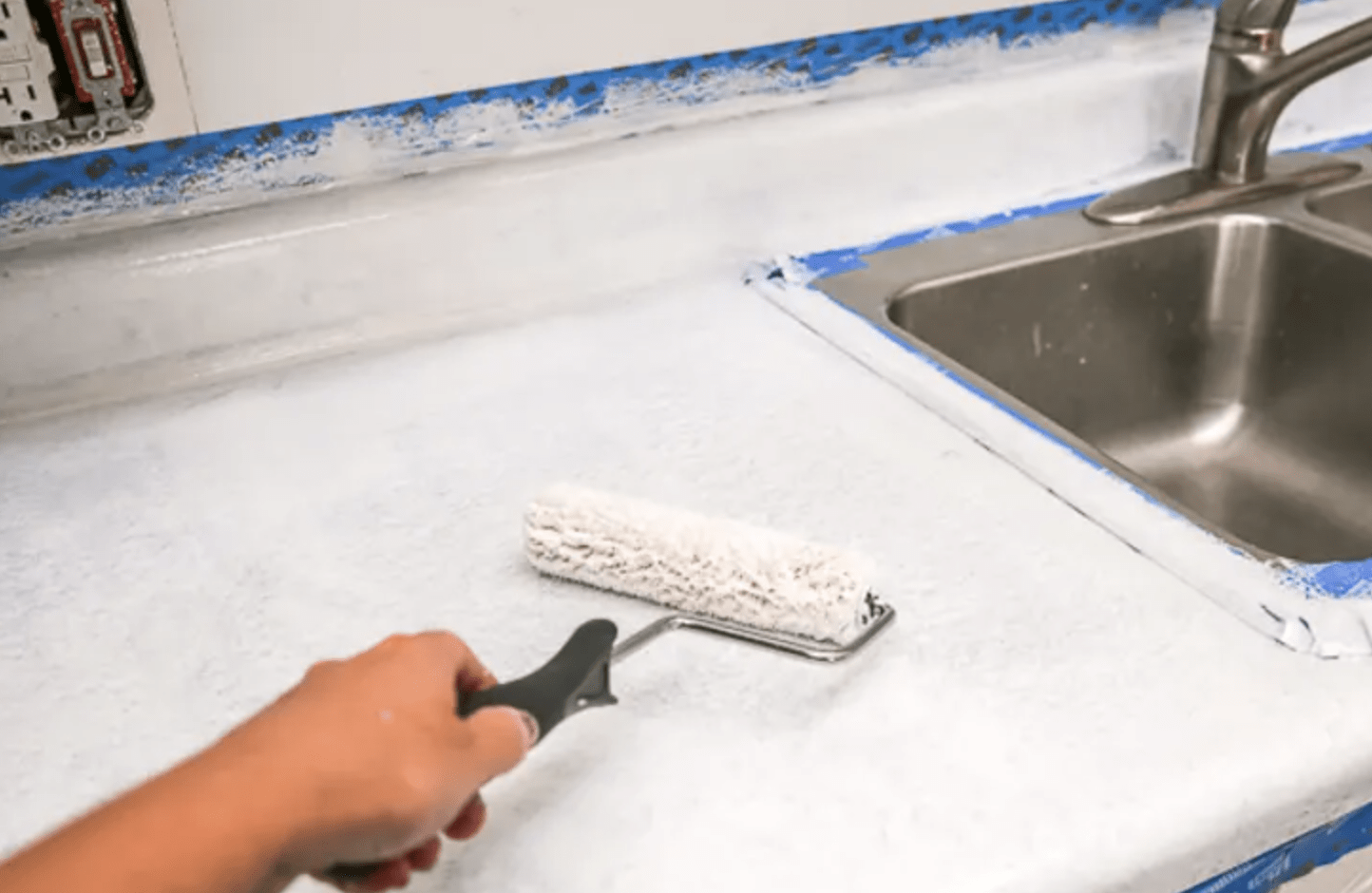 White roller painting on countertop stainless steel sink.