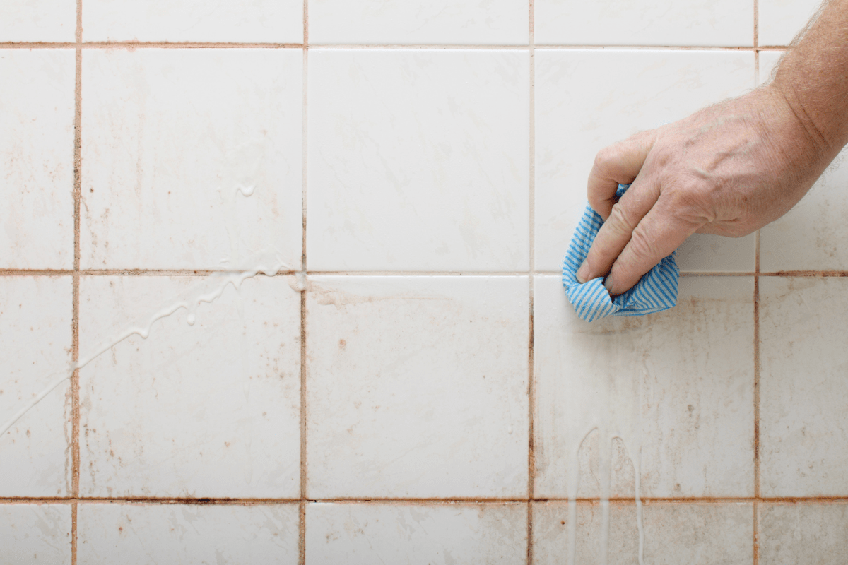 close up of hand scrubbing tile with soap scum blue cloth