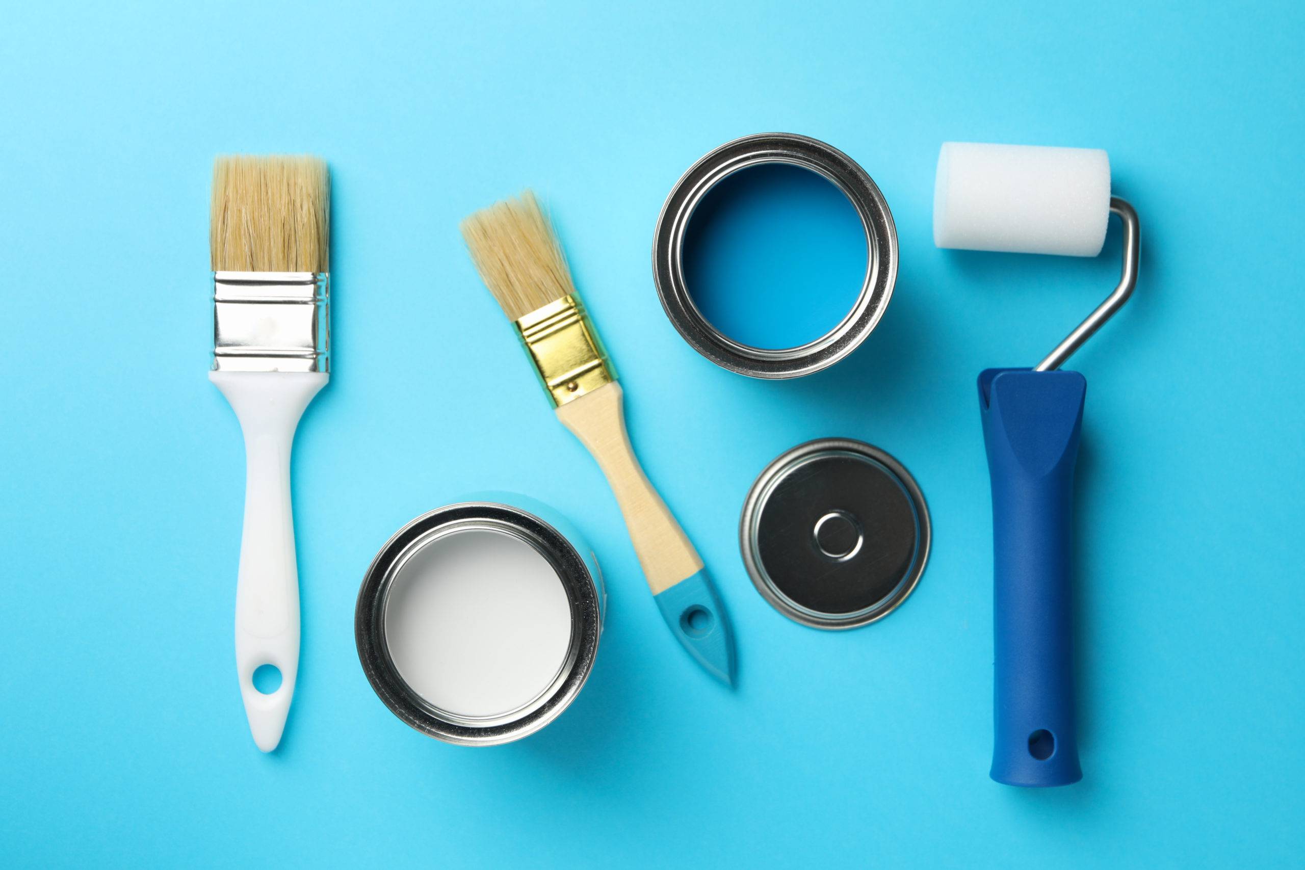 Paint cans, brushes and roller on blue background, top view