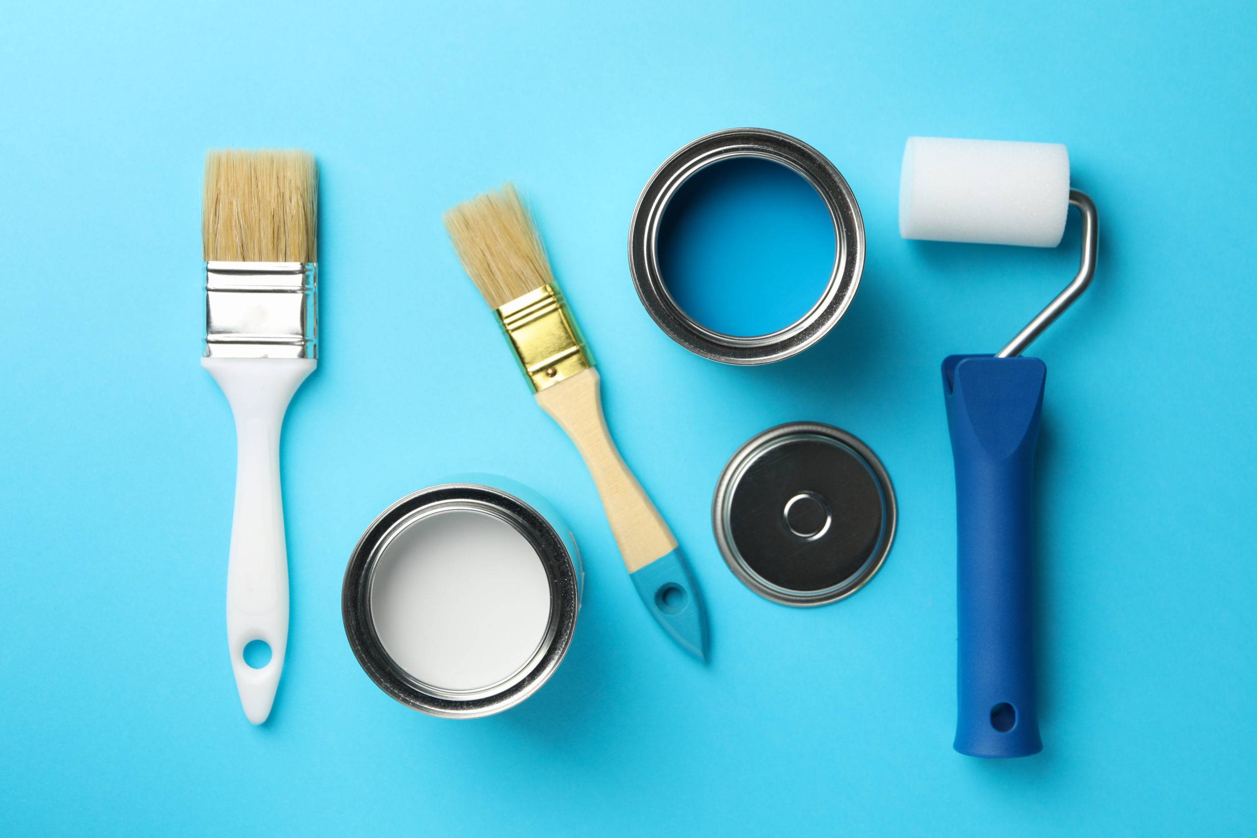 Paint cans, brushes and roller on blue background, top view.