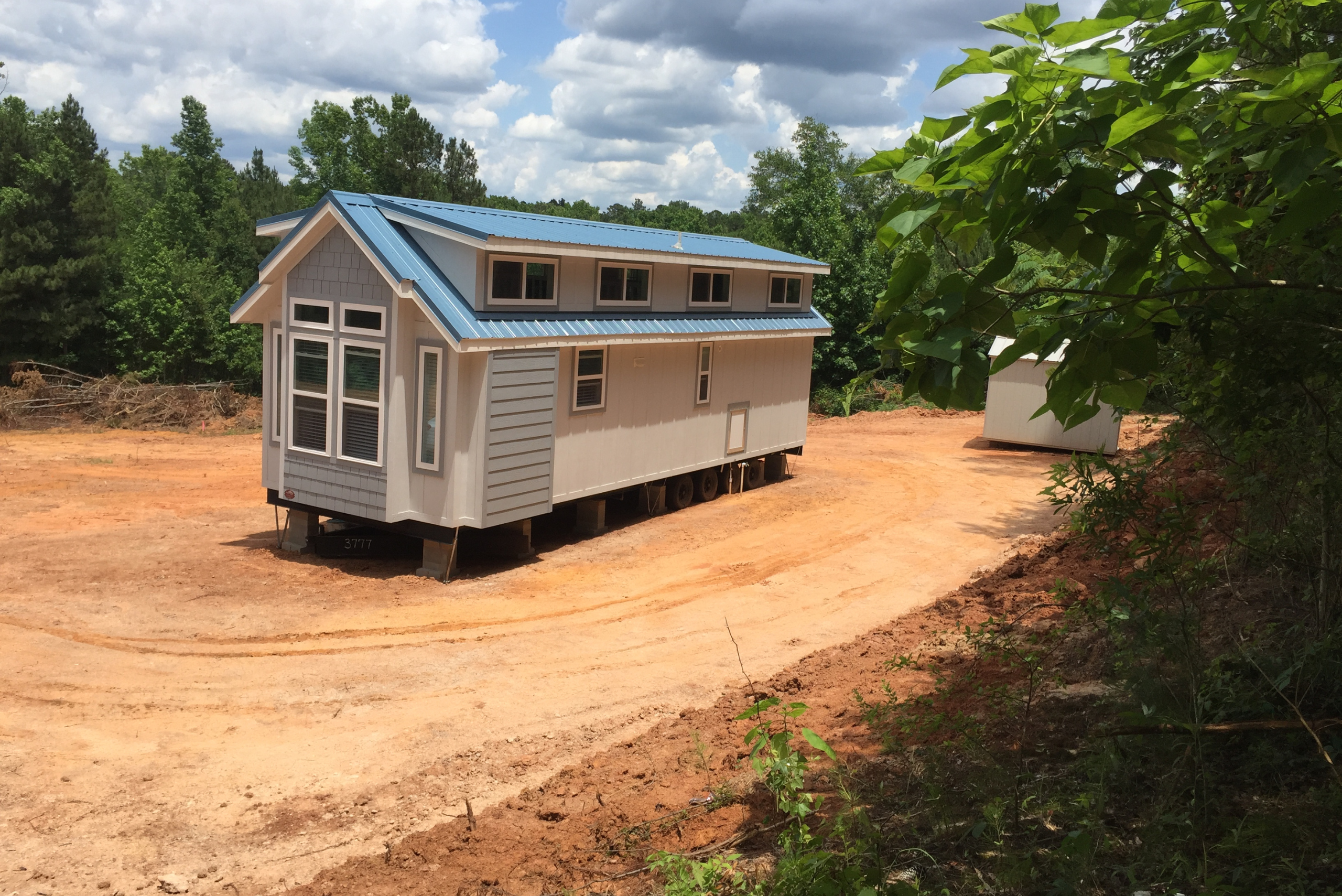 Tiny home on a dirt patch flanked by a shed.