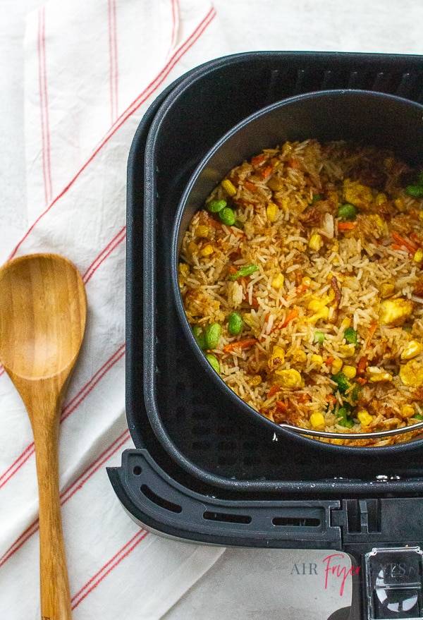 vegetable fried rice in a black square air fryer bin with a wooden spoon on the table