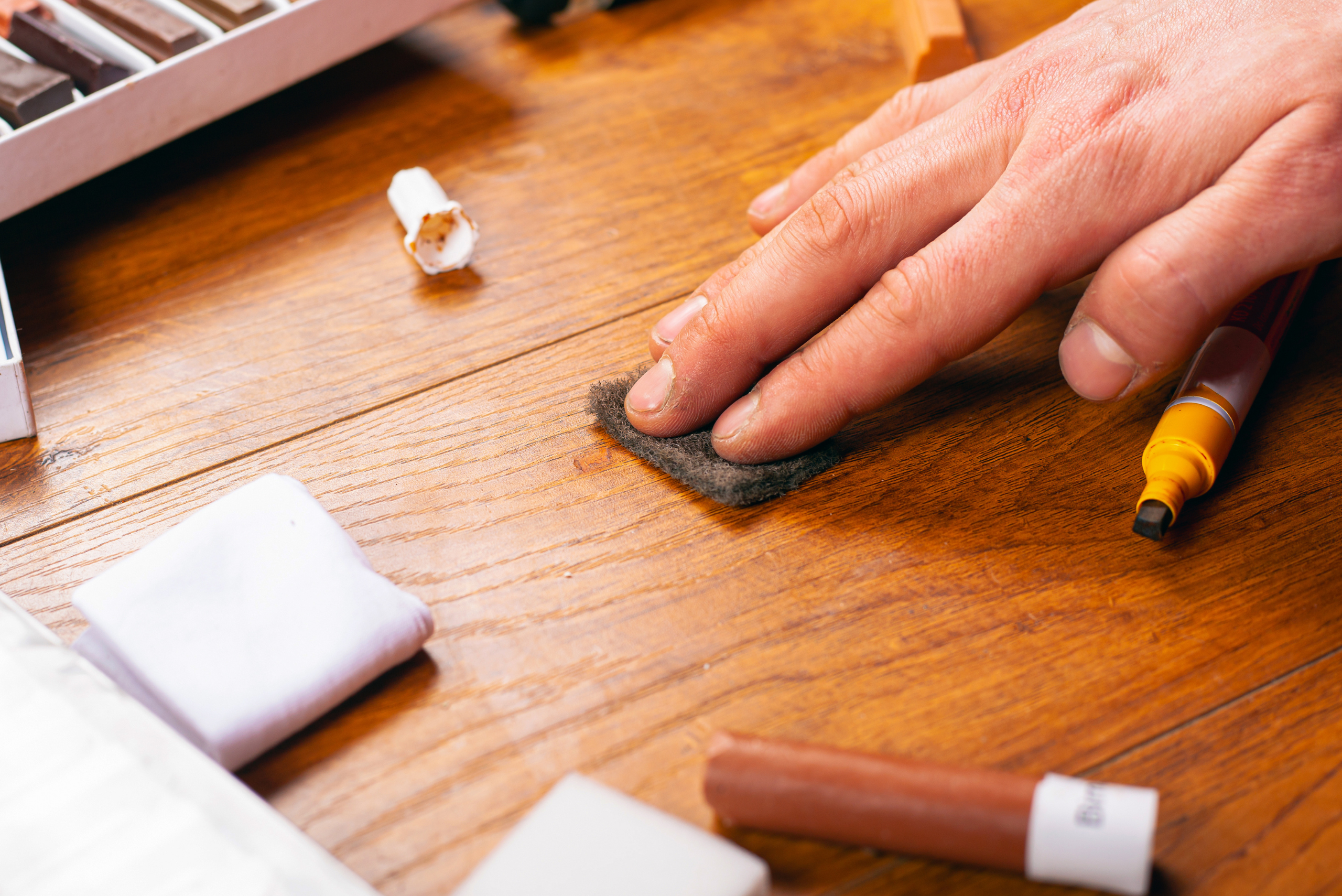 Hand using steel wool to remove scratches from hardwood.