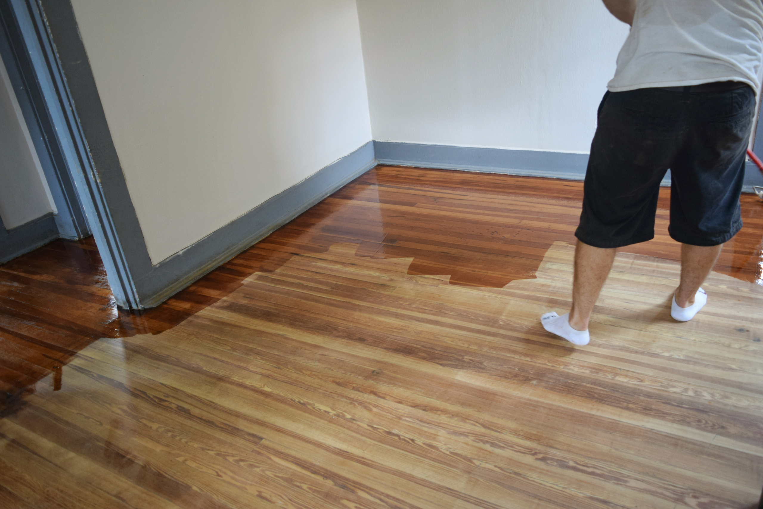 Person staining hardwood flooring using a roller.
