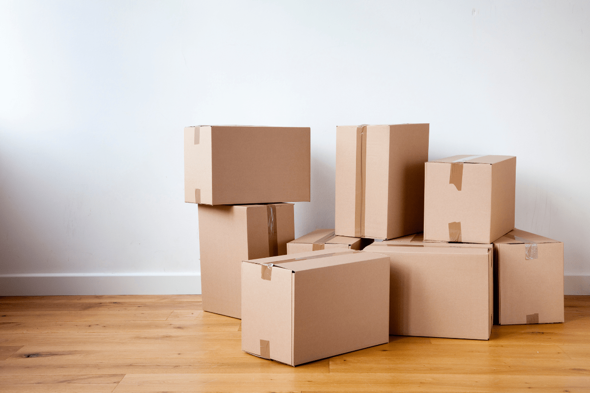stack of cardboard moving boxes on wood floor against white walls