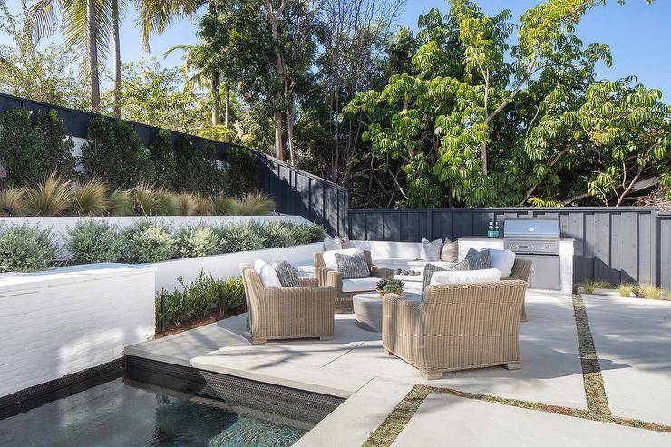 outdoor patio with wicker chairs and shrub garden next to pool 