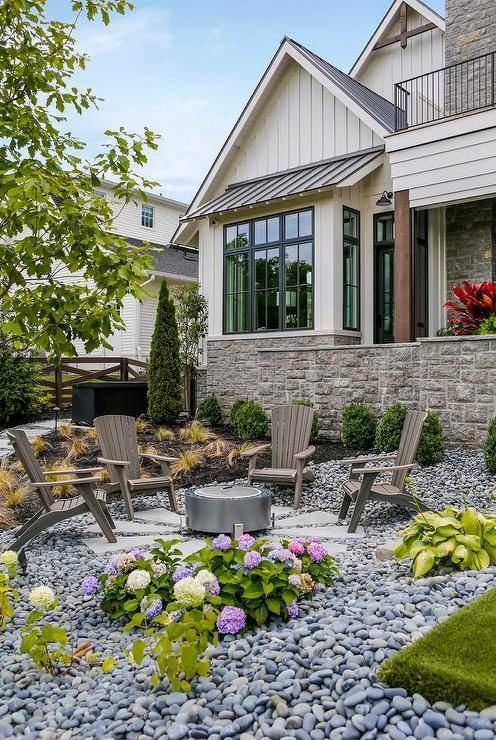 backyard firepit setup with metal circular fire pit, wooden Adirondack chairs, colorful flower arrangements and a stone garden surrounding