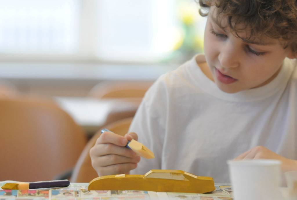 kid works on painting pinewood derby car