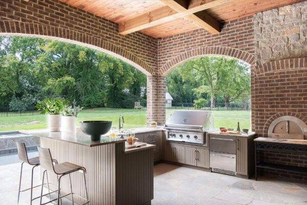ourdoor kitchen on brick patio with high bar stool chairs and eat in island, stainless steel bbq and appliances with wood fire pizza oven 