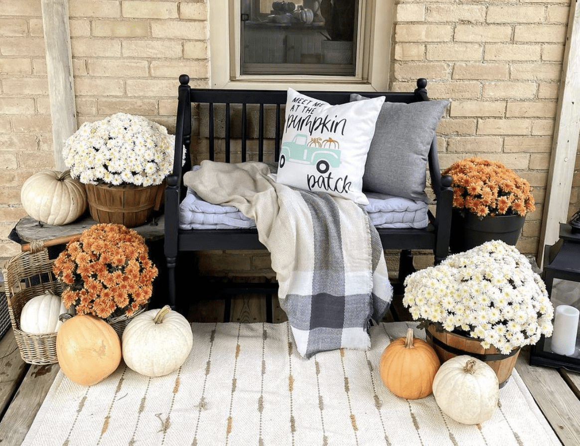 wooden black bench on fall front porch setting with pumpkins and white & orange flowers