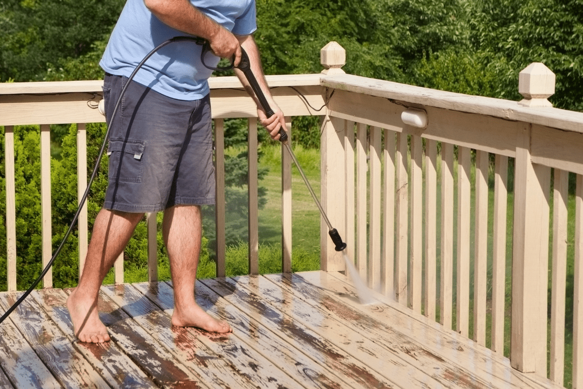 man in shorts and bare feet standing on old wood deck using pressure washer