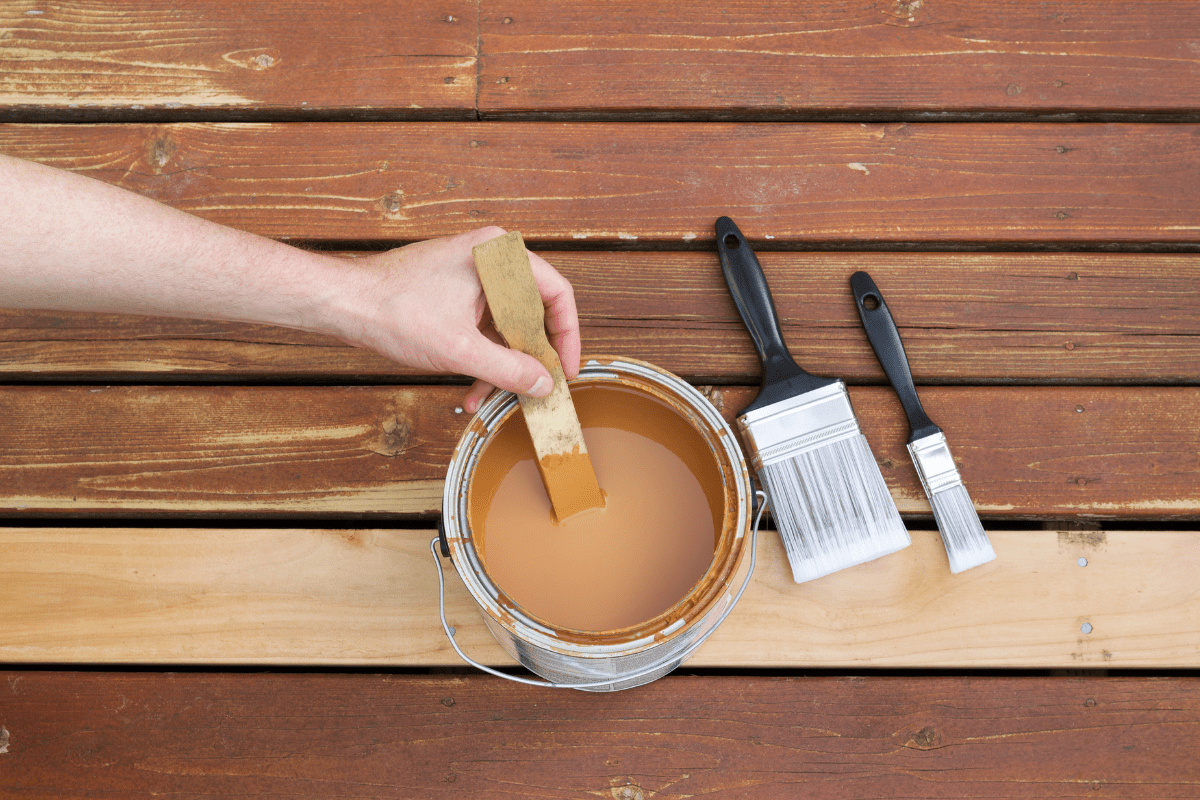 man's hand stirring paint can full of wood stain on deck outside