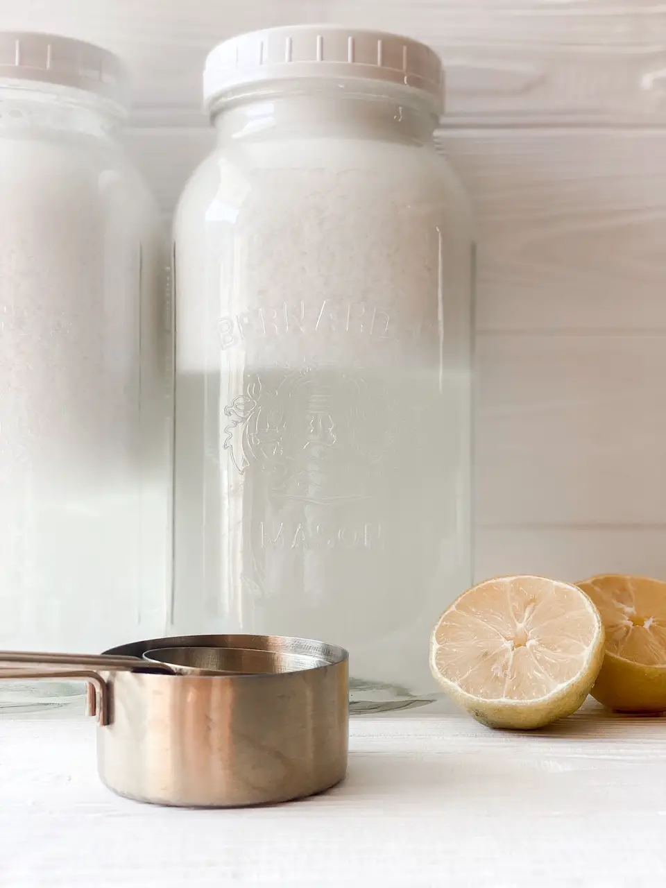 close up of clear liquid in mason jar with bronze measuring cups and cut lemon