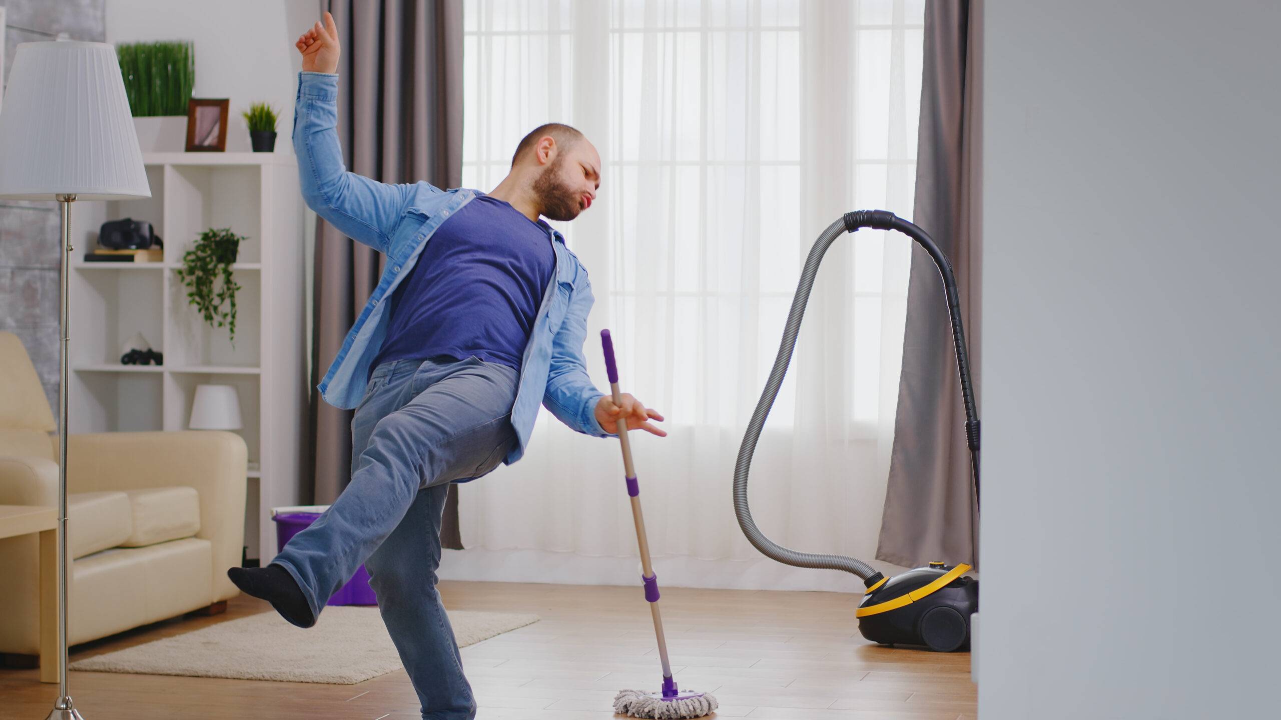 man in jeans and blue shirt dancing while swiffering floor