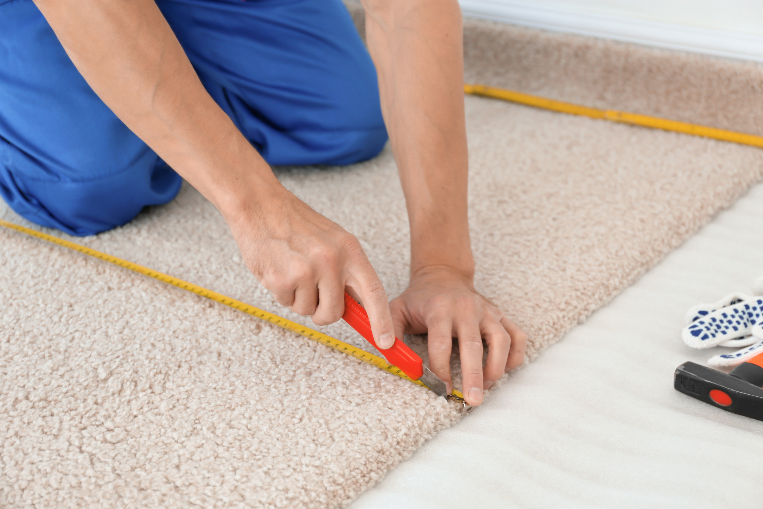 Worker using utility knife and measure tape edge to cut the carpet in a straight line.