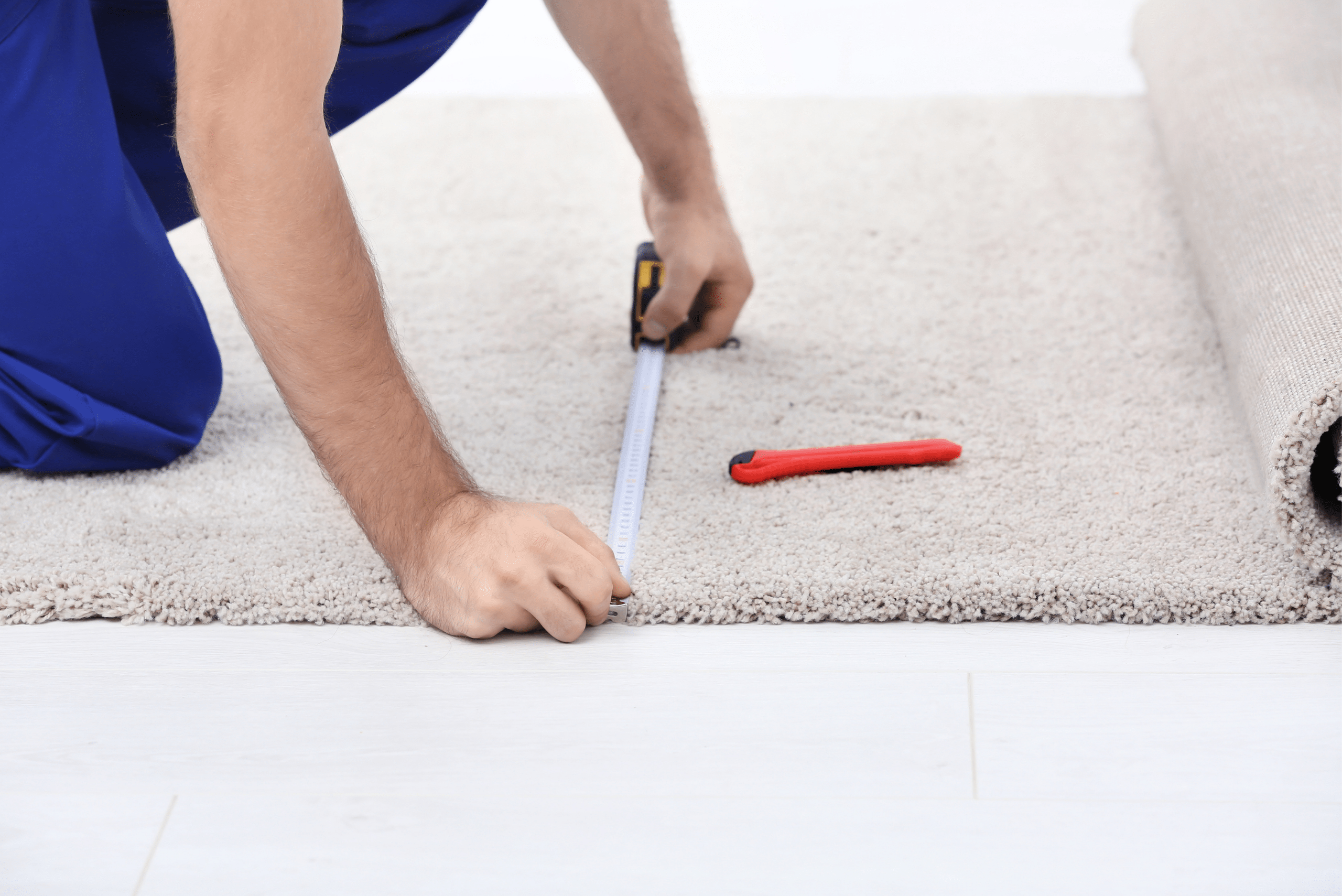Worker measuring carpet with red utility knife on carpet.